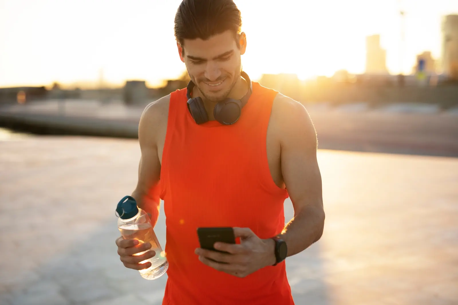 A smiling man in a running vest checking his phone after a sunset workout