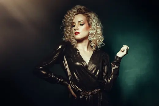 A studio portrait of a woman with curled hair under dramatic side light