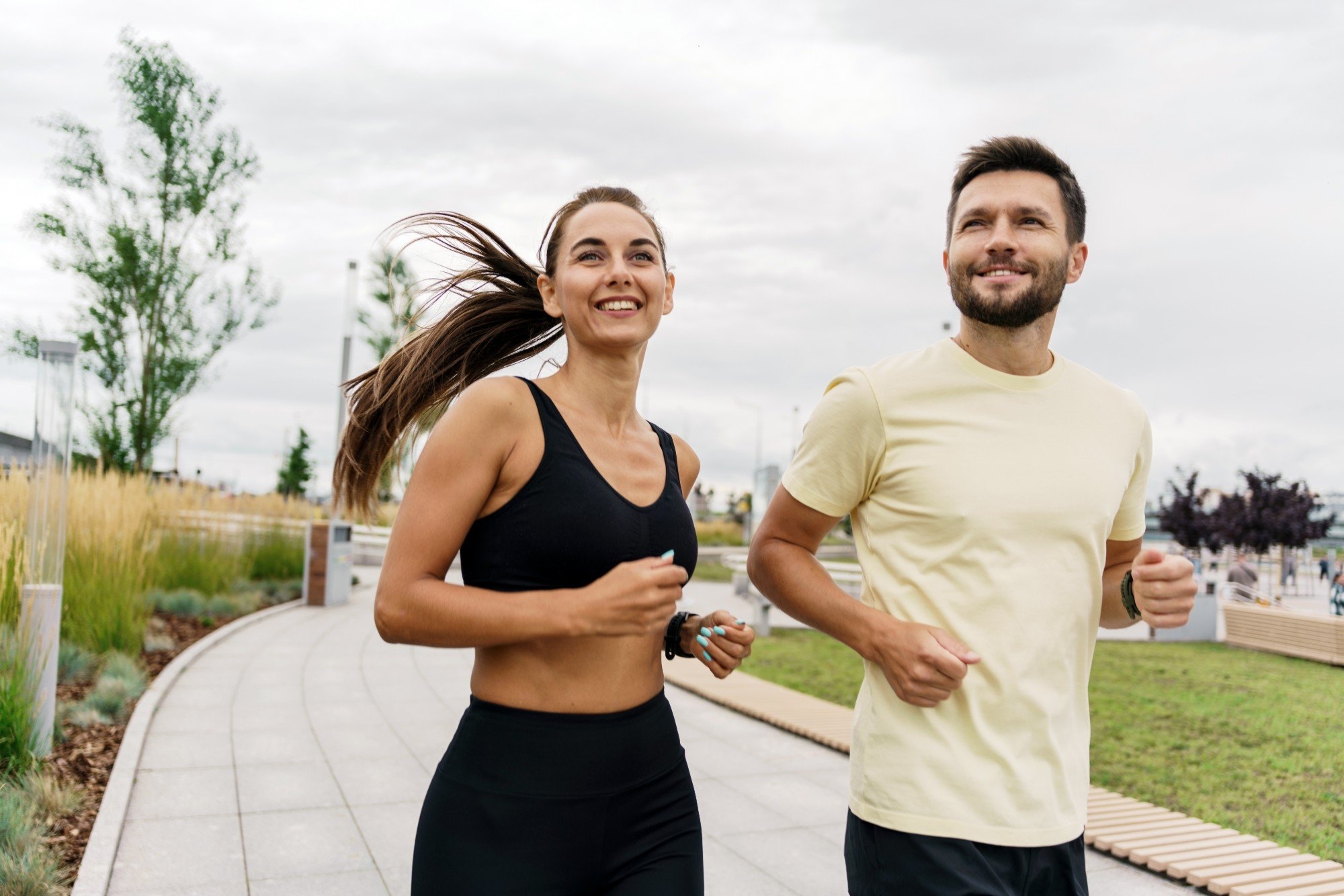 A smiling woman and man jogging side by side along a park path
