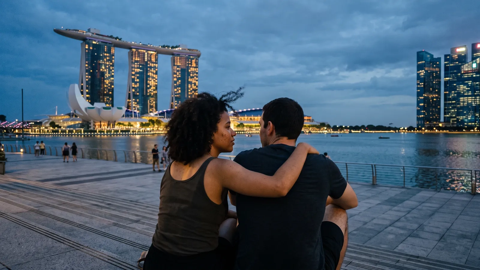 A couple sits on the waterfront steps at Marina Bay at blue hour, the lit Singapore skyline reflected in the water in front of them (AI-generated image)
