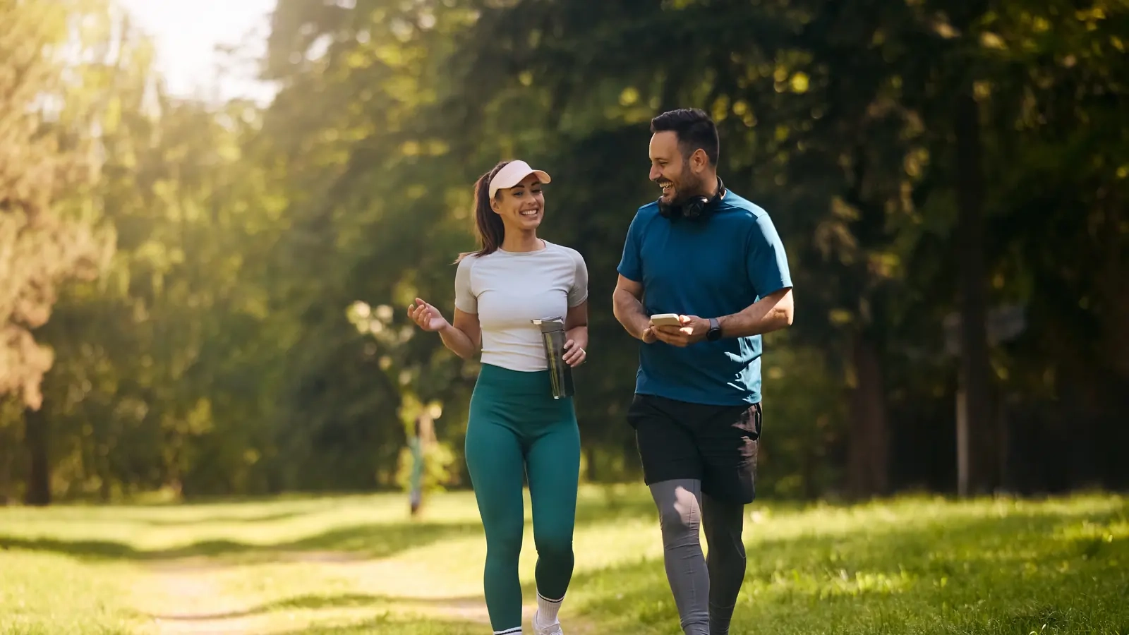 A smiling man and woman walking and chatting along a sunny park path