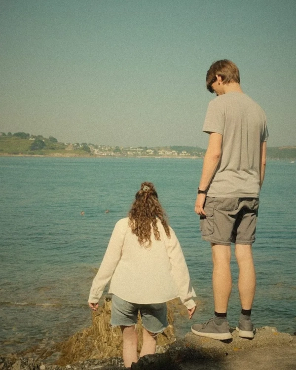 Parent and child standing on rocks by the sea, seen from behind