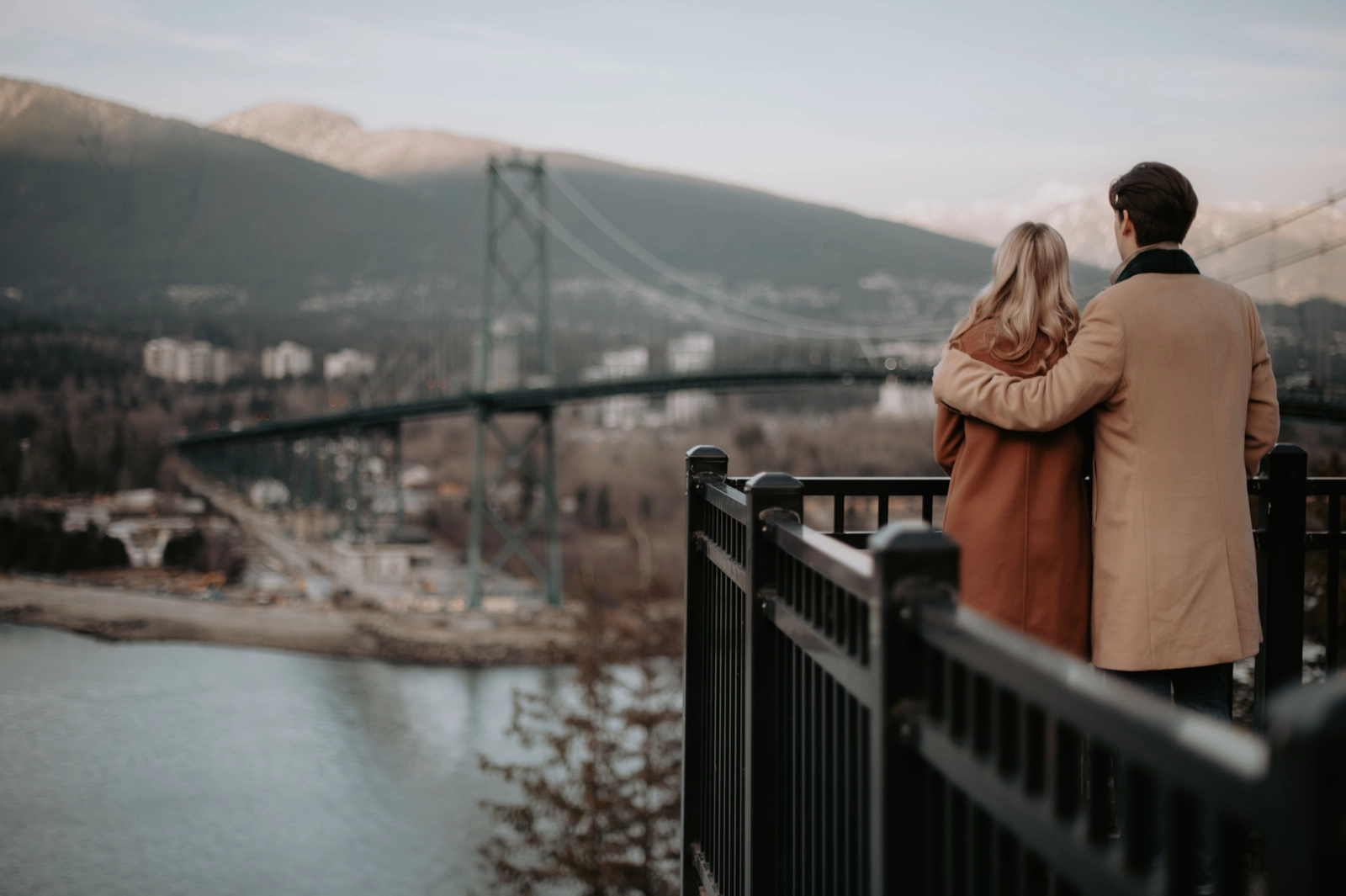 Couple at a railing overlooking a suspension bridge and mountains