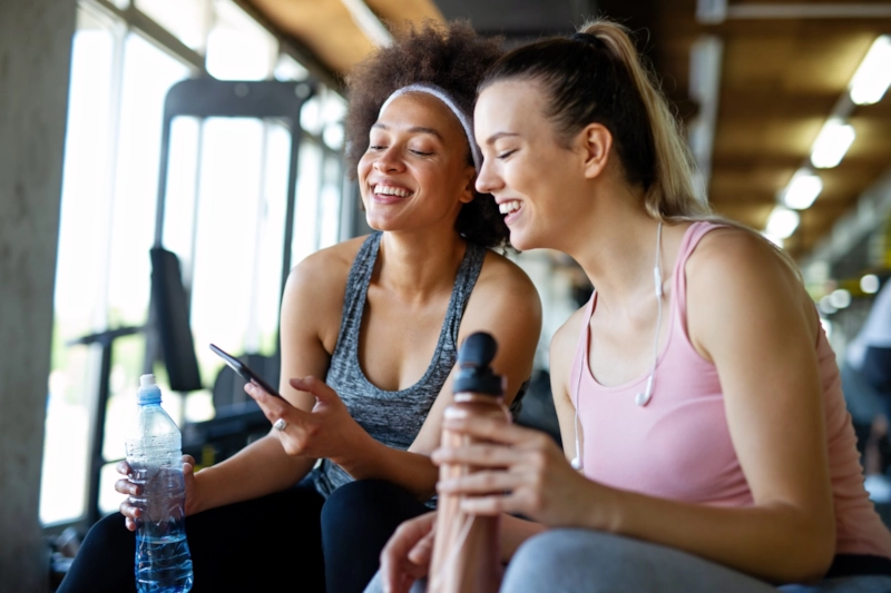 Two smiling women at the gym looking at a phone together
