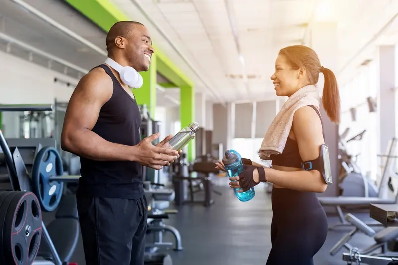 A man and woman chatting with water bottles in a bright gym