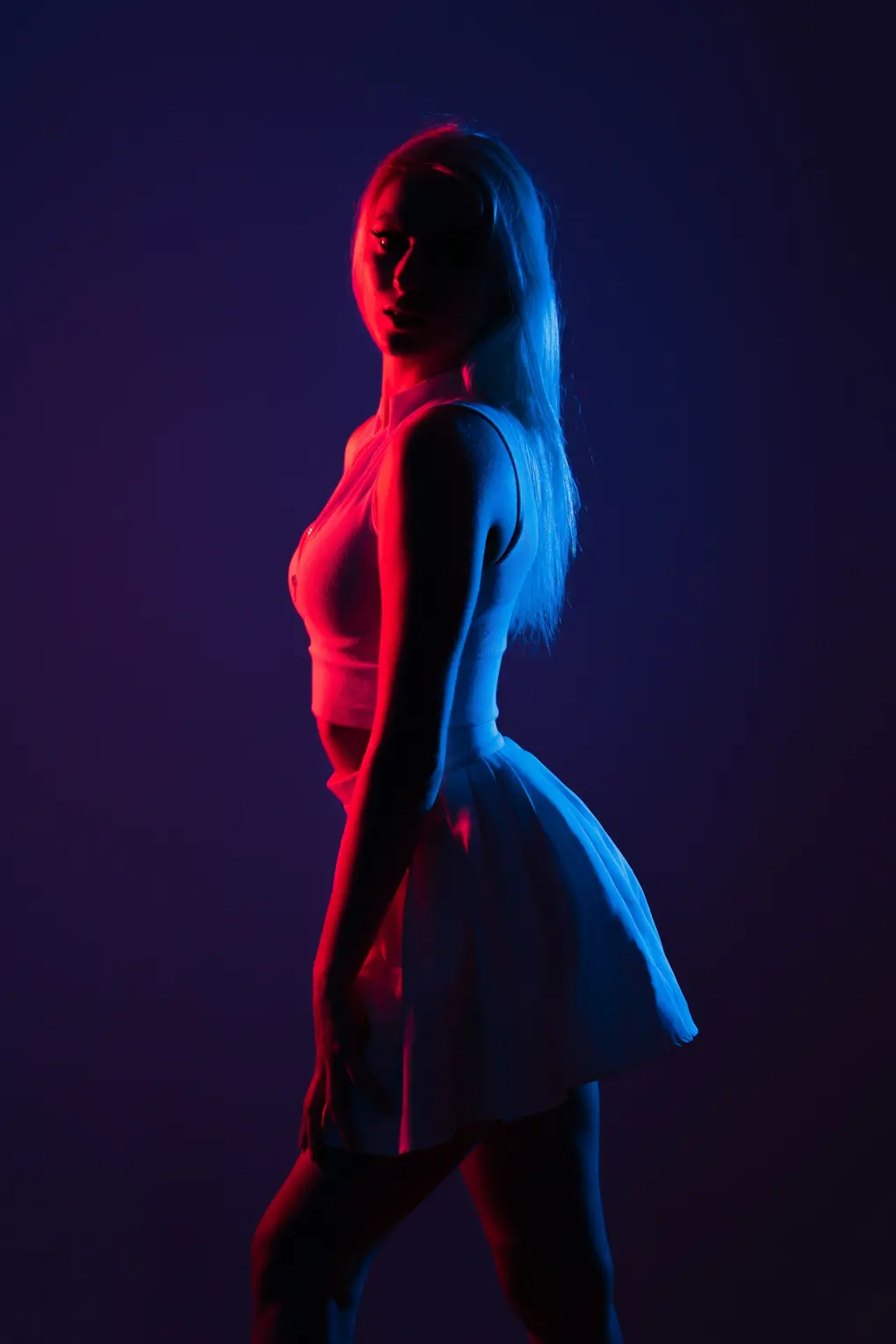 Silueta de una persona con vestido, recortada contra una luz azul y magenta.