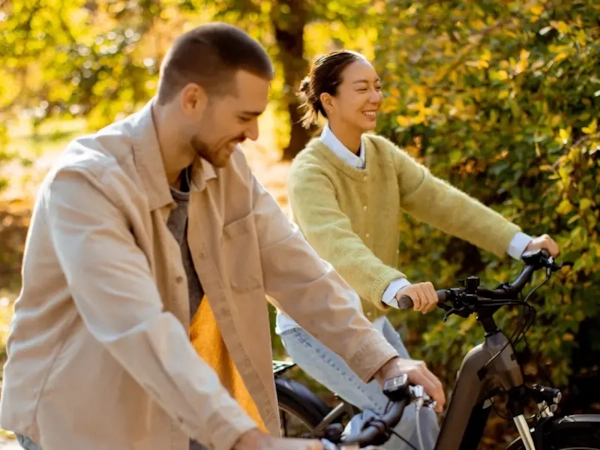 A smiling couple riding bikes together along a sunny autumn woodland trail