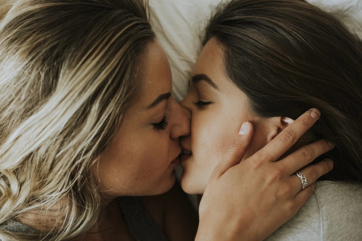 Two women kissing, lying close together in bed