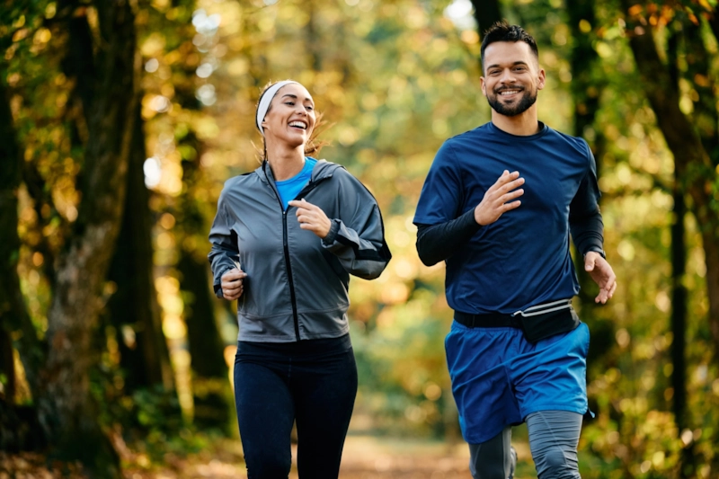 A laughing woman and man jogging together through autumn woods