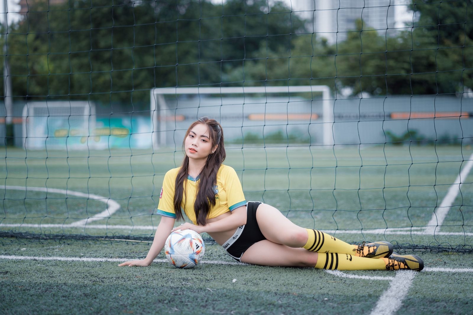A woman in a yellow kit lying on a pitch beside a football