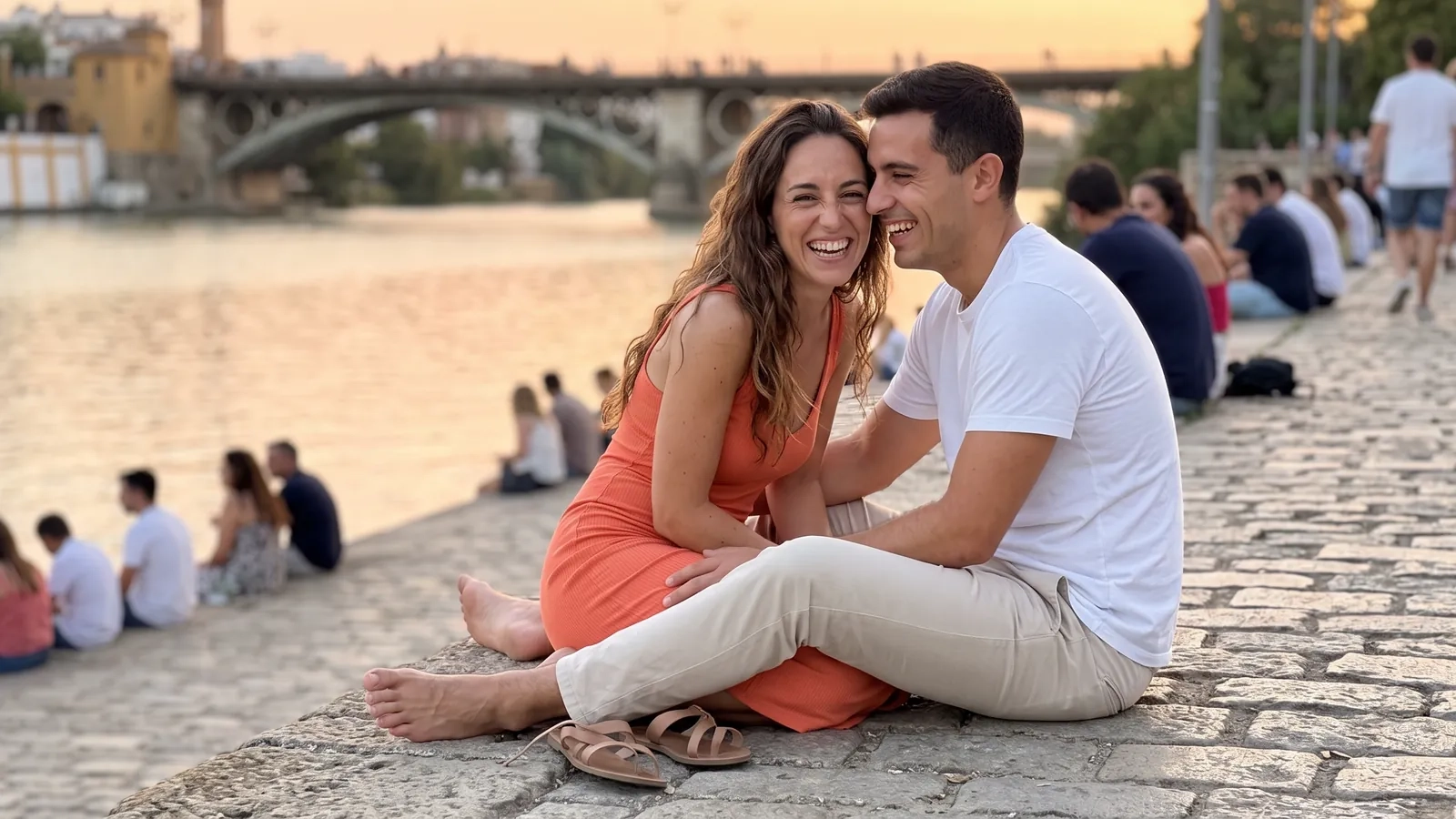 Una pareja se ríe sentada a la orilla del Guadalquivir en Sevilla al atardecer, con el puente de Triana al fondo (imagen generada por IA)