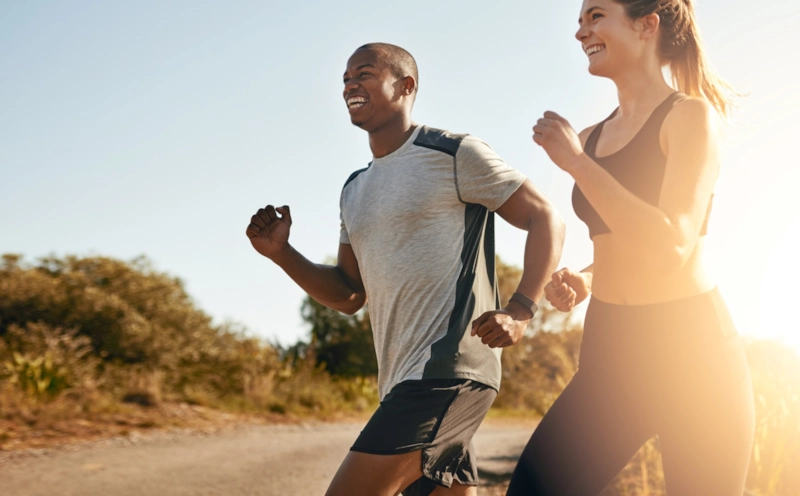 A smiling man and woman jogging together in bright sunshine