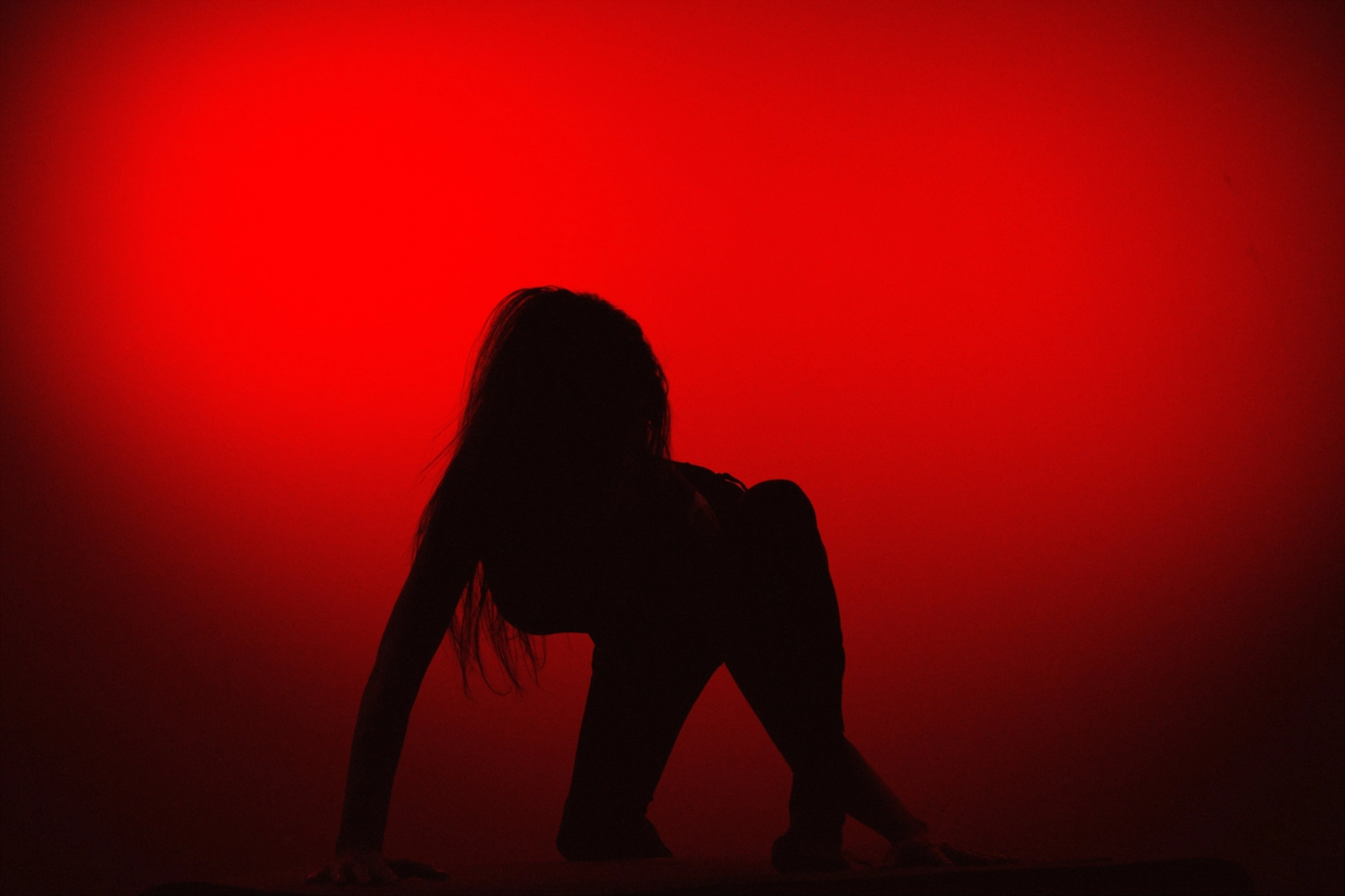 Silueta de una persona agachada sobre un fondo rojo intenso