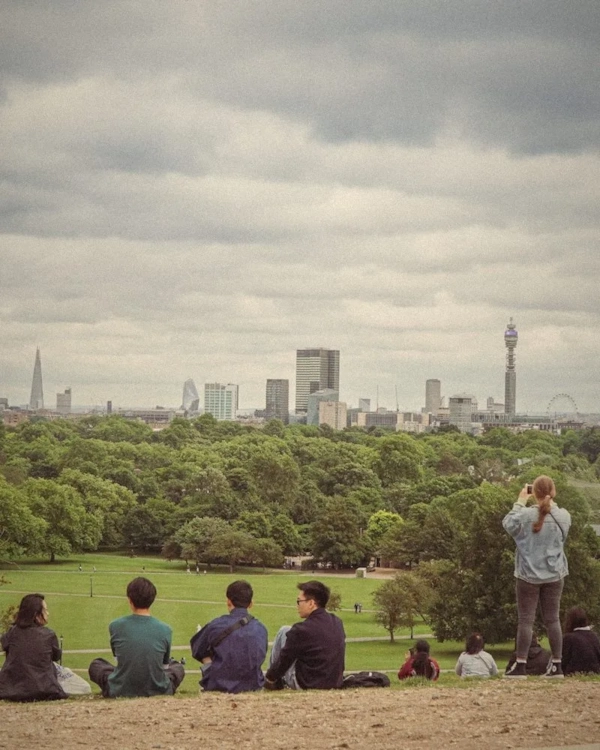 People relaxing on a hill in a London park with the skyline behind