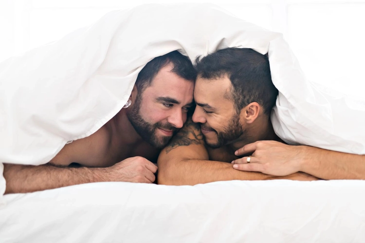 Two gay men looking at each other while laying in bed