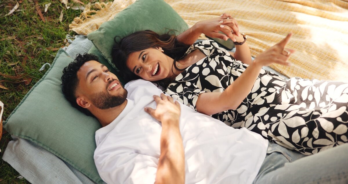 A happy couple lying on a picnic blanket on the grass, laughing together in warm afternoon sunlight