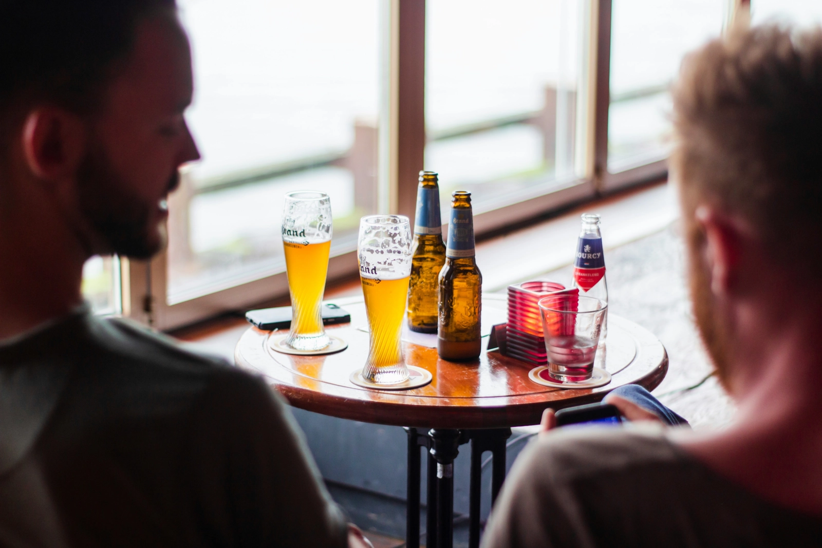 Dos hombres charlando en la barra de un bar, de espaldas.