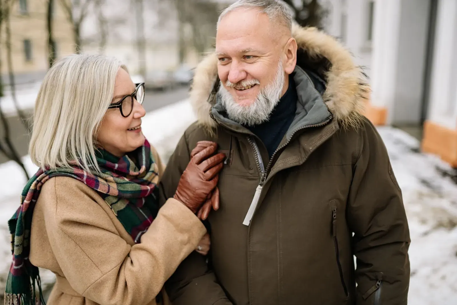 A smiling couple in warm winter coats, arm in arm on a snowy day