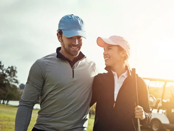 A smiling couple in golf caps standing arm in arm beside a golf cart