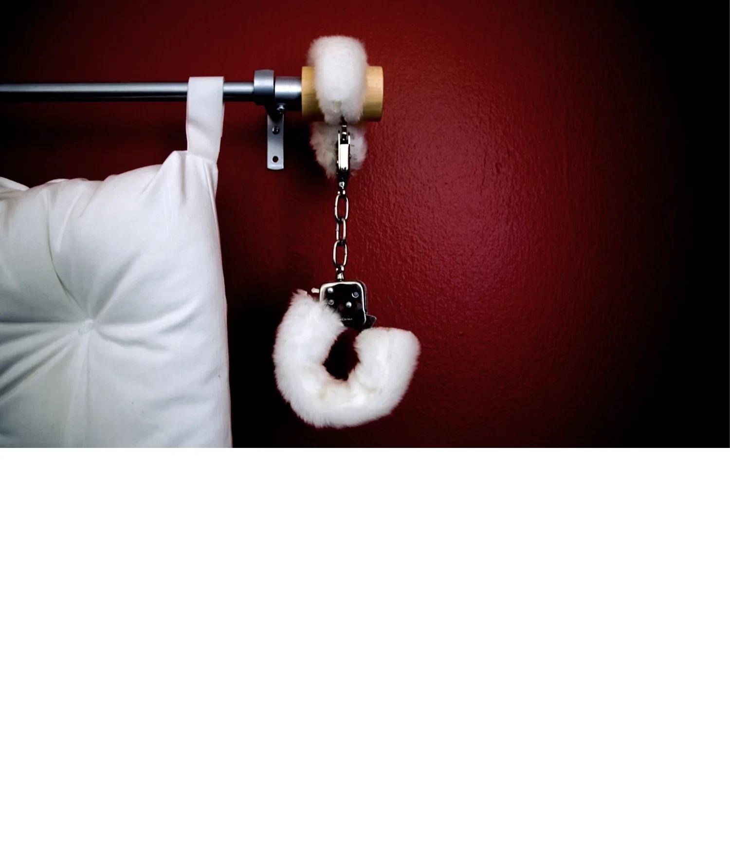 Esposas de peluche blanco colgadas junto a un cabecero acolchado sobre una pared roja, foto ilustrativa de archivo