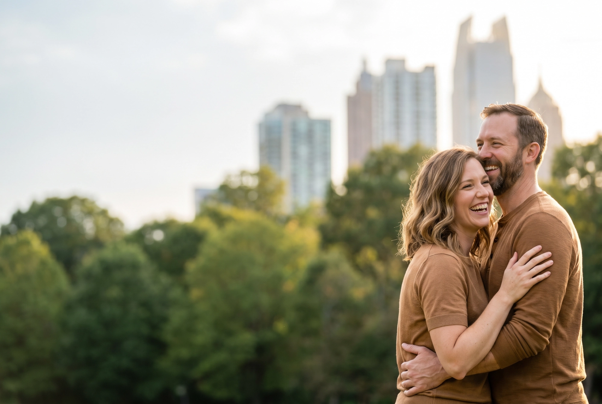 A happy couple laughing together in an Atlanta park with the Midtown skyline behind them