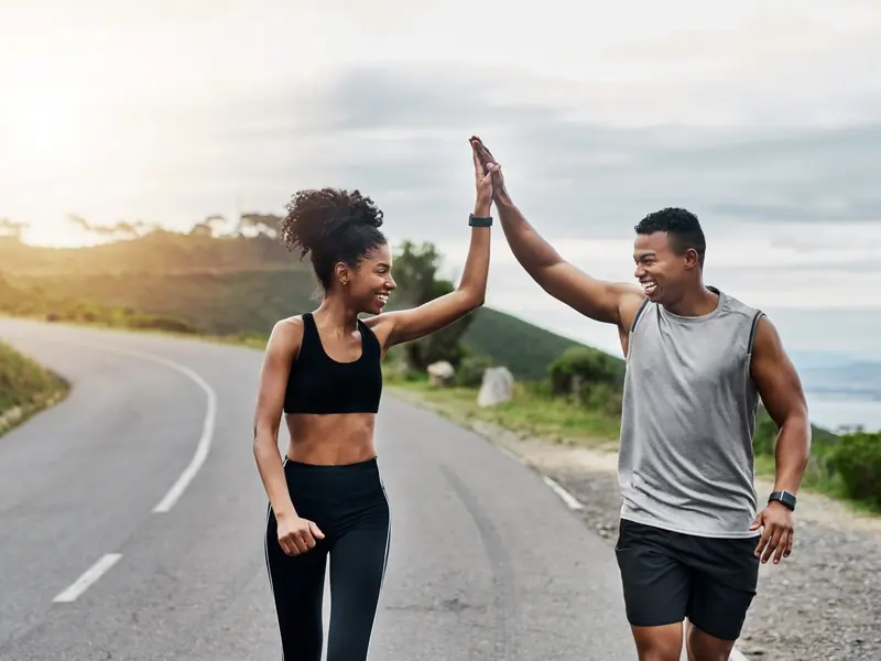 A woman and a man high-fiving mid-run on a coastal road
