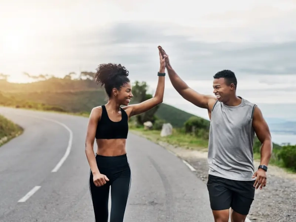 A woman and a man high-fiving mid-run on a coastal road