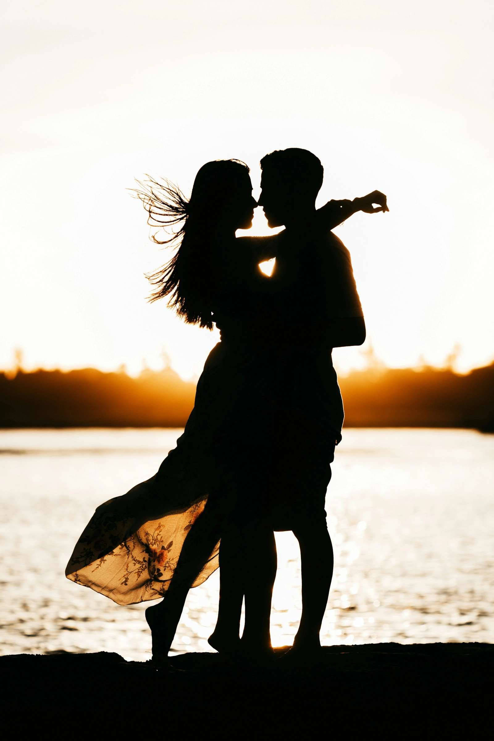 Pareja en silueta, abrazada frente al mar al atardecer.