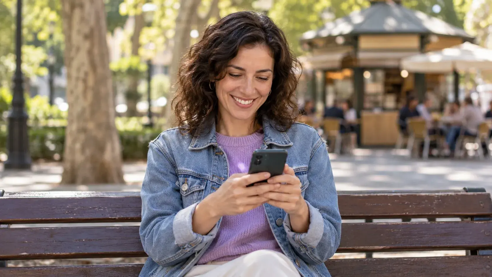Persona sonriente en un banco de un parque mirando su móvil antes de proponer una cita