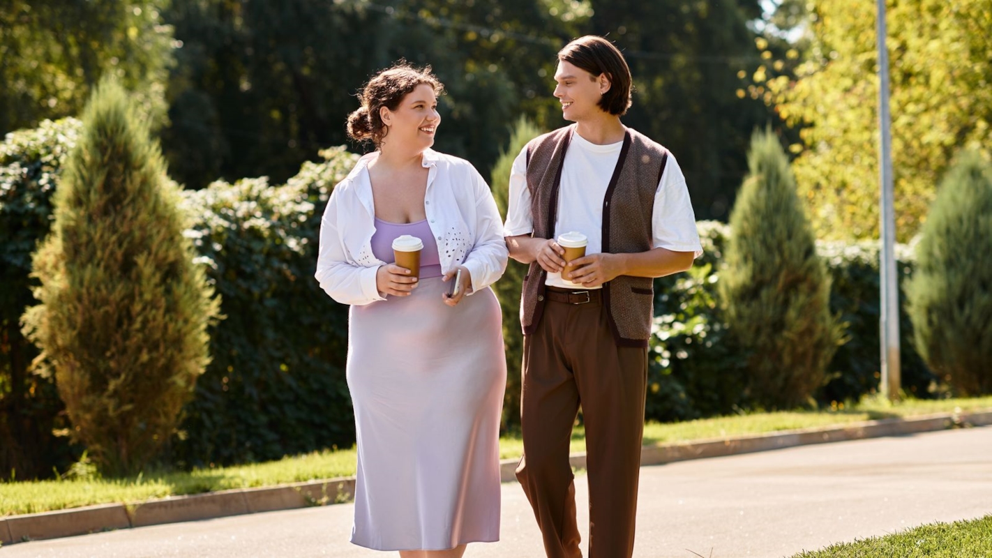A couple walking together outdoors, laughing and holding coffee cups