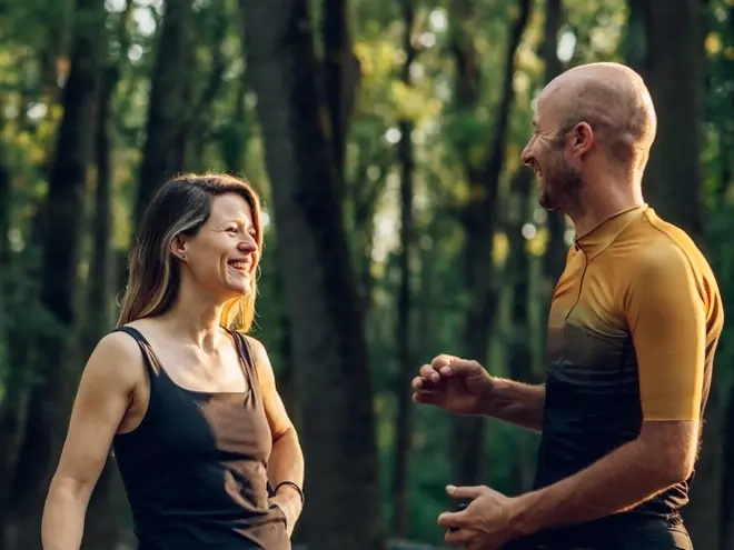 A woman and man laughing together beside their road bikes in a forest