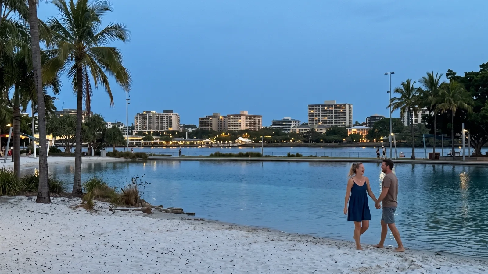 A couple walks hand in hand along the sand of Streets Beach in South Bank, Brisbane, at dusk, palm trees and the city lights behind them (AI-generated image)