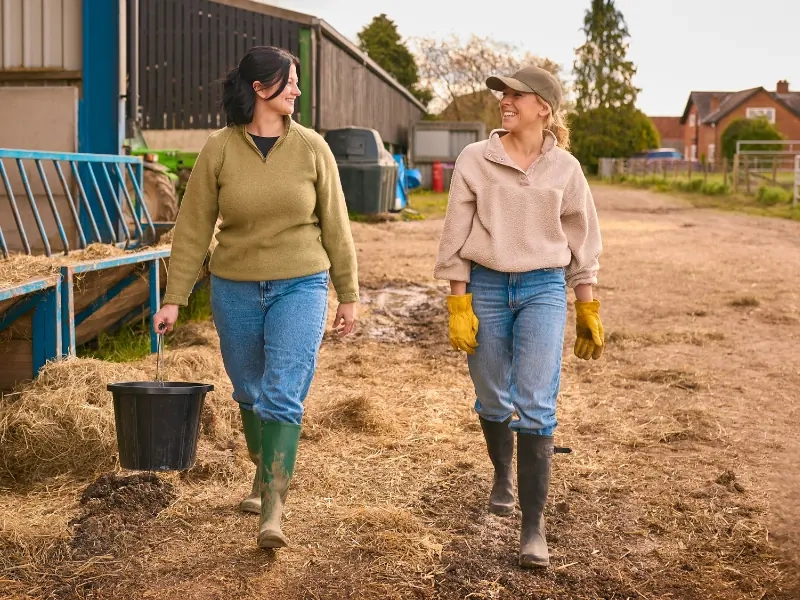 Two women walking together across a farmyard