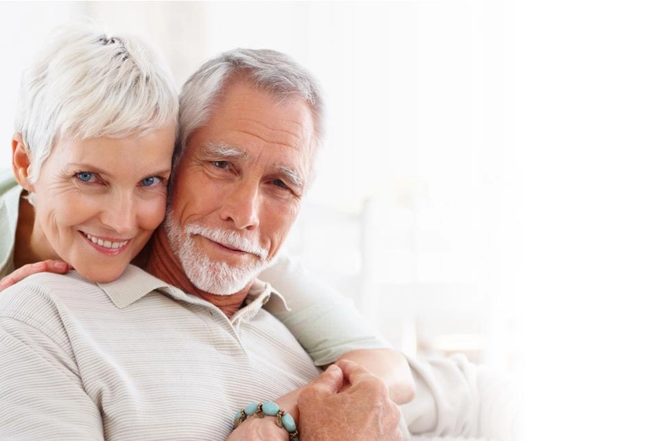A smiling silver-haired couple, her arm around his shoulders