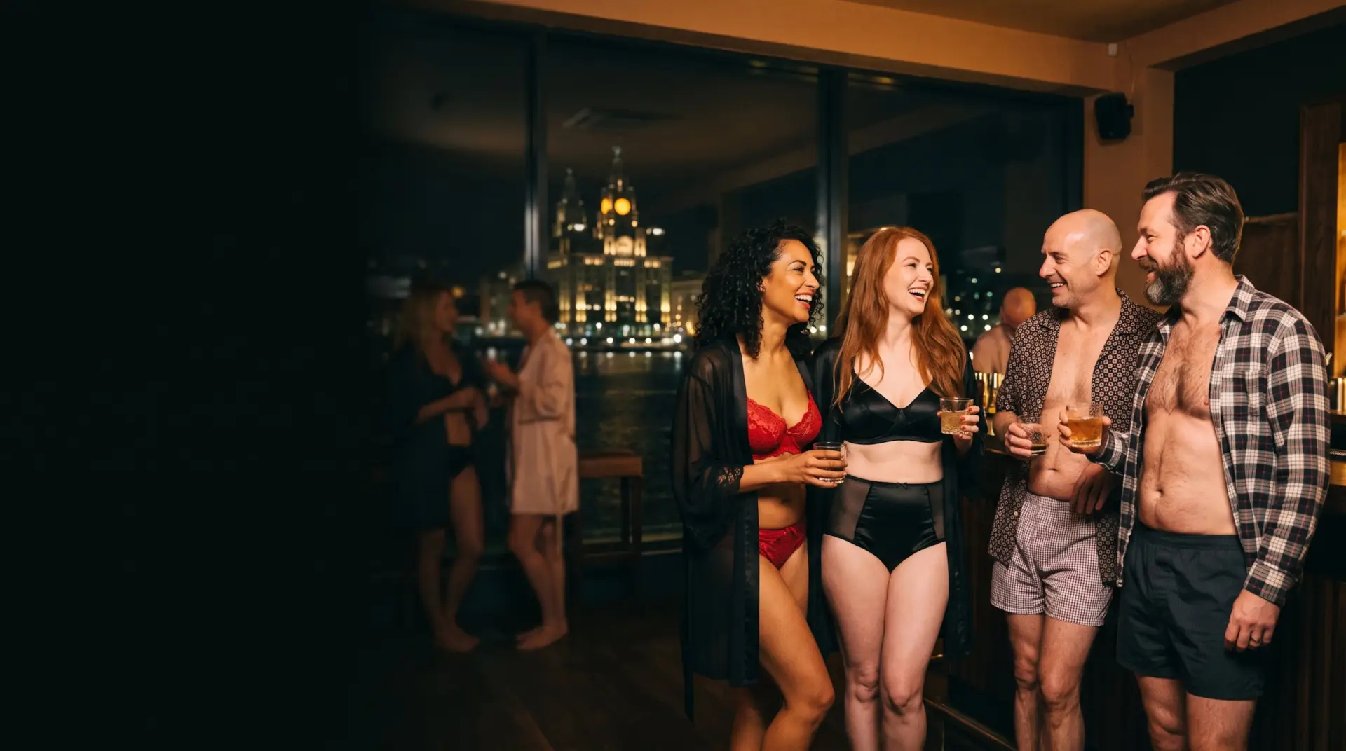 Two couples laughing at the bar, the Liver Building lit up across the waterfront