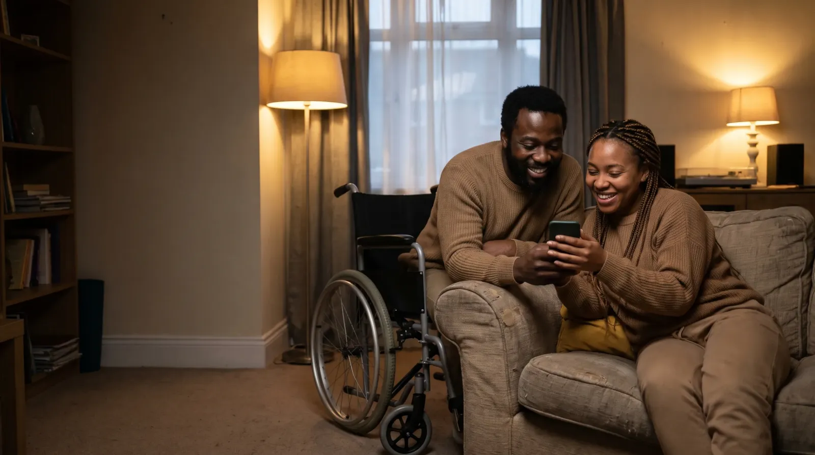 A couple on a sofa at home reading a message on a phone together, the woman's wheelchair beside them