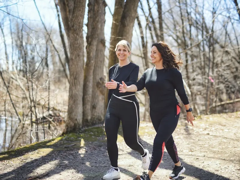 Two women walking briskly and chatting on a sunny woodland path