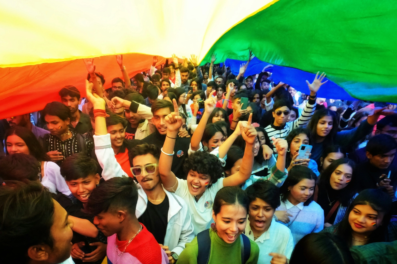 Multitud celebrando bajo una gran bandera arcoíris.