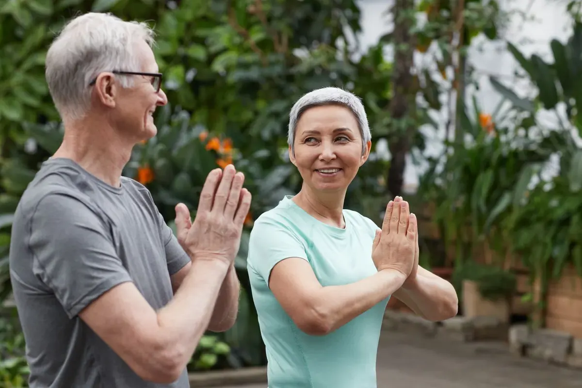 A smiling couple in sports tops doing a yoga stretch together in a leafy garden