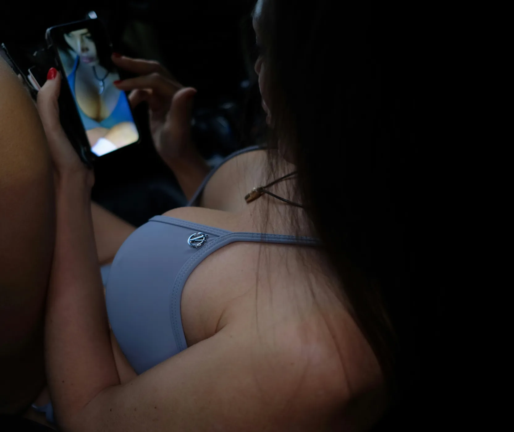 Unas manos sosteniendo un celular con una foto abierta en la pantalla, por encima del hombro desnudo de otra persona.