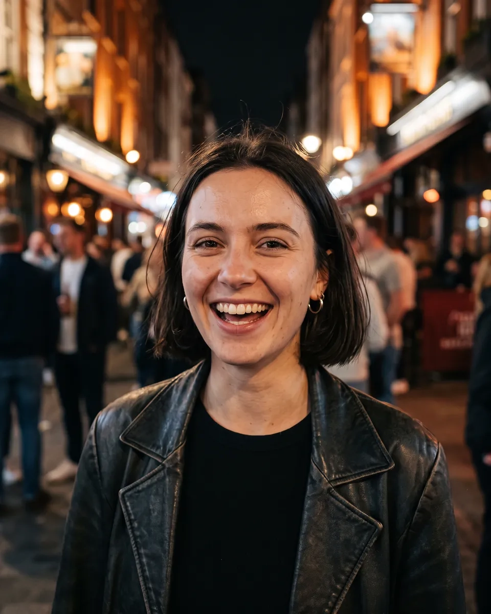 A woman with a sleek brown bob, a black top and a leather jacket laughs on a busy Soho street at night, bar lights glowing behind her (AI-generated image)