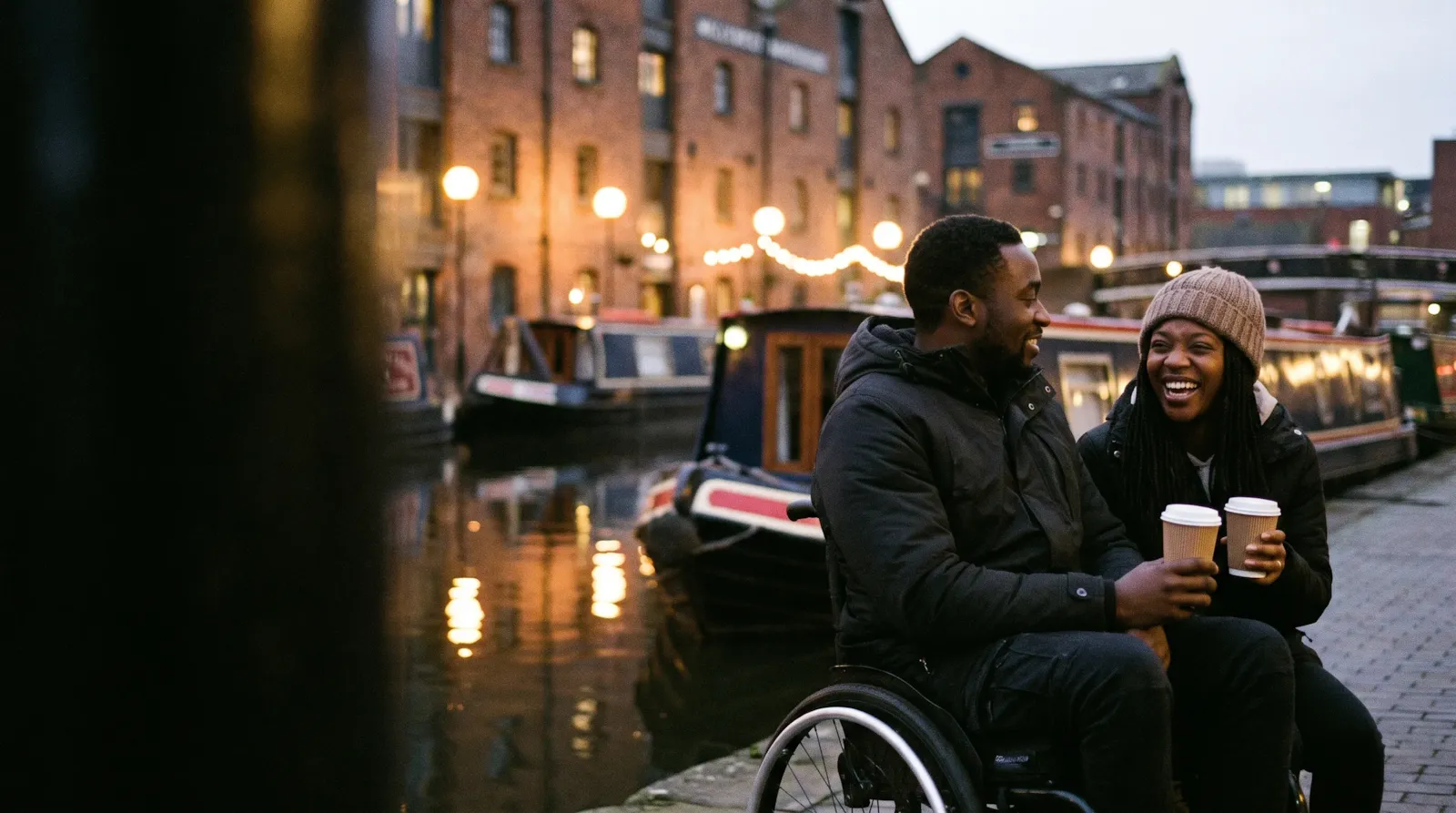 A couple laughing over coffees beside the narrowboats at Gas Street Basin in Birmingham; the man is a wheelchair user
