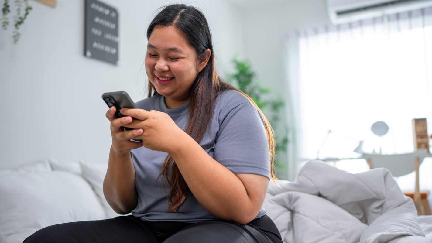 A woman sitting at home, smiling while looking at her phone