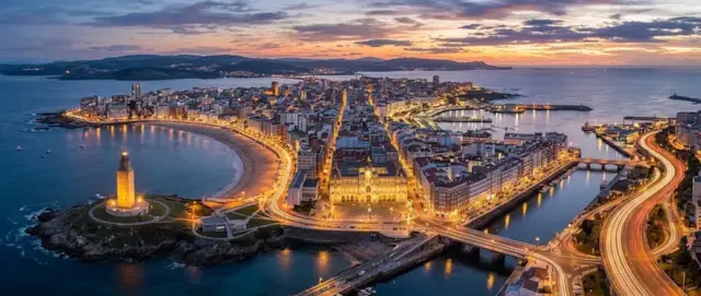 A Coruña al anochecer con la Torre de Hércules, la playa y la ciudad iluminada junto al mar
