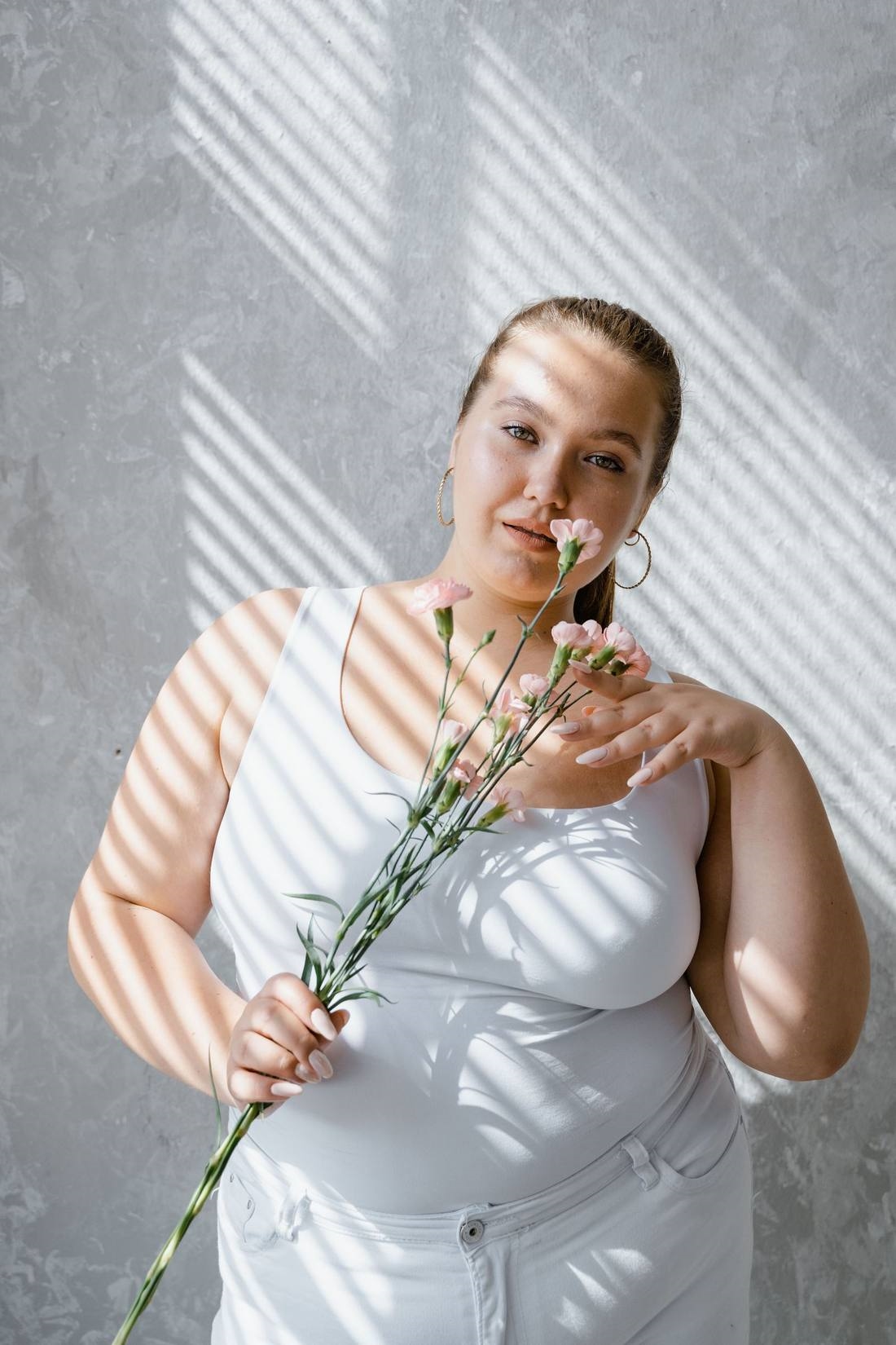 Mujer curvy sonriente con flores, foto ilustrativa de stock, no representa a un miembro real