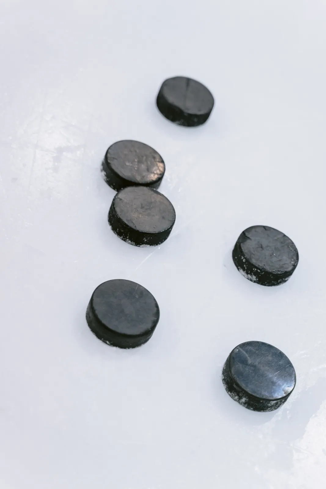 Six rondelles de hockey noires éparpillées sur une glace blanche