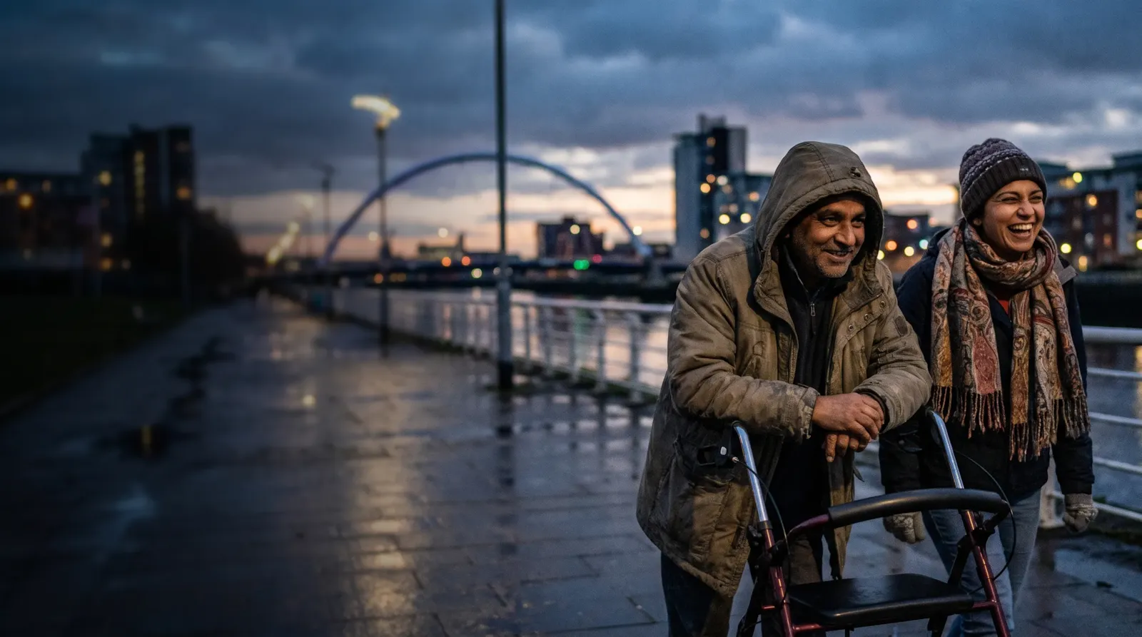 A couple laughing beside the River Clyde at dusk; the man has cerebral palsy and walks with a rollator