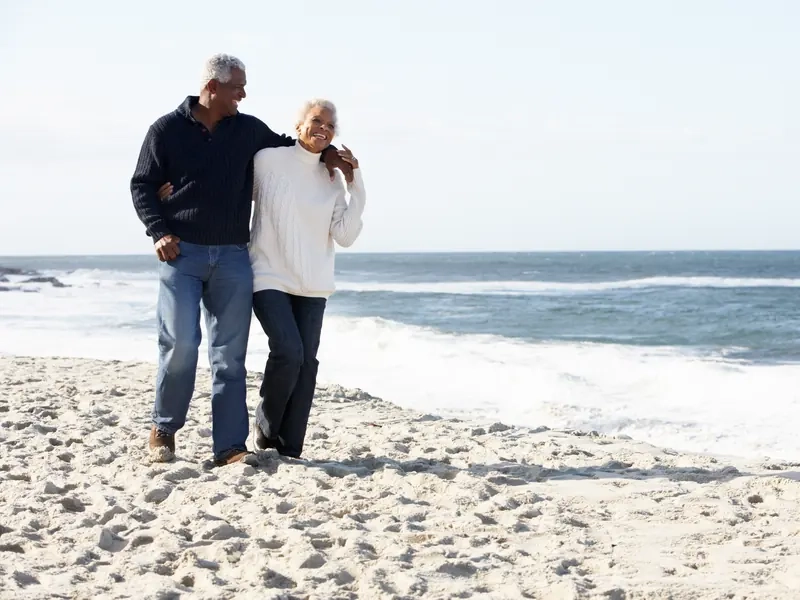 A laughing older couple walking arm in arm along a sandy beach