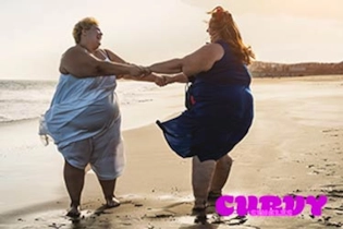 Happy lesbian BBW couple walking together on the beach