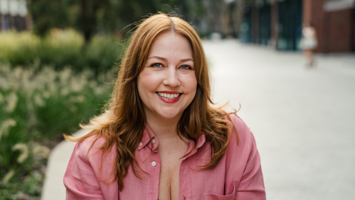 A woman smiling outdoors in a pink shirt